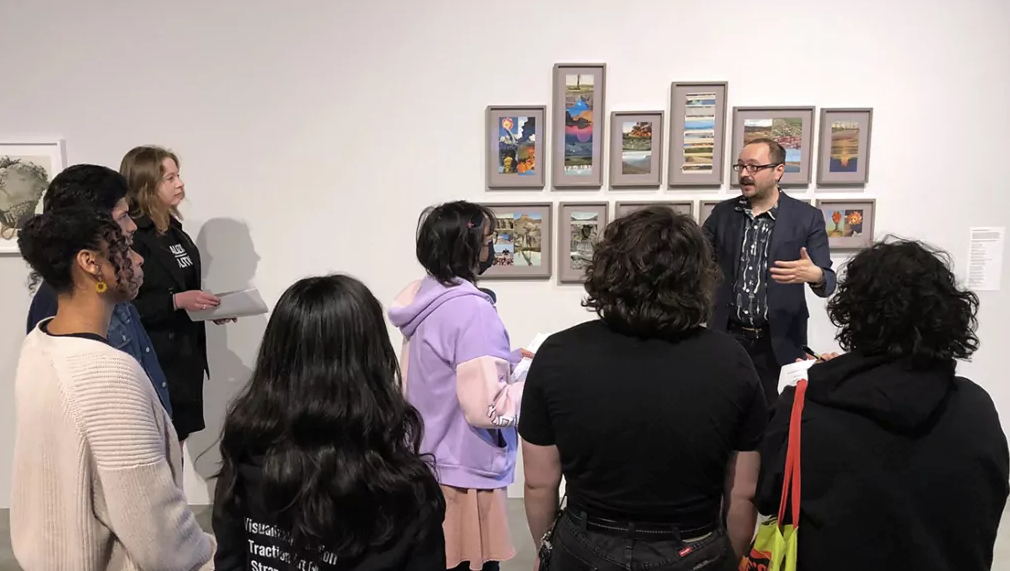 Man in suit jacket stands talking in front of group of students